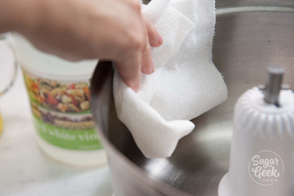 Hand wiping down a metal bowl with a paper towel.