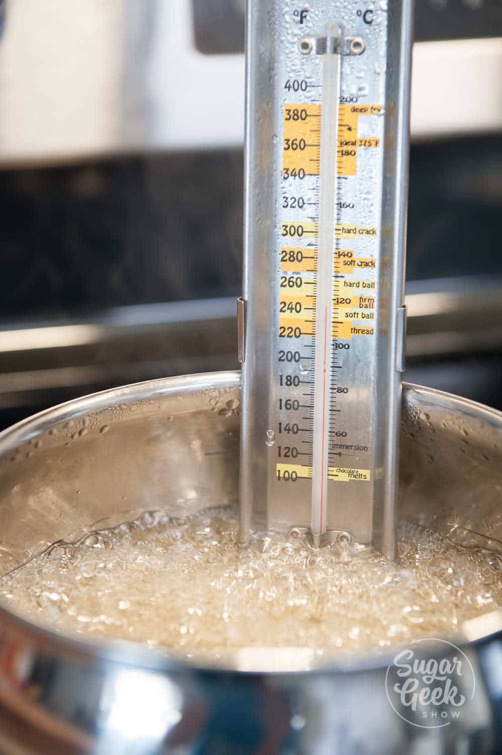 Candy thermometer inserted into a metal pot of boiling sugar.