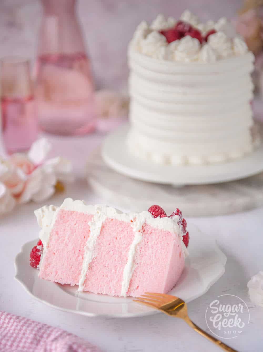 slice of pink velvet cake on a white plate in front of pink velvet layer cake in the background