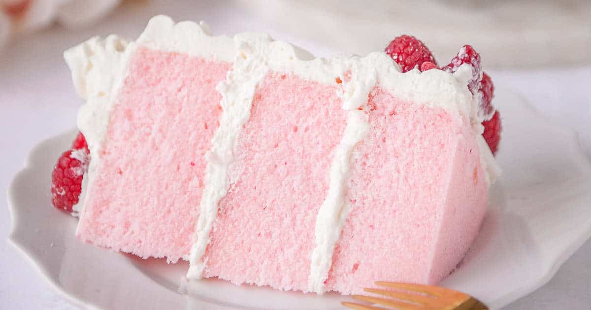 slice of pink velvet cake on a white plate with fresh raspberries