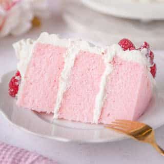 slice of pink velvet cake with whipped cream frosting and fresh raspberries on a white plate