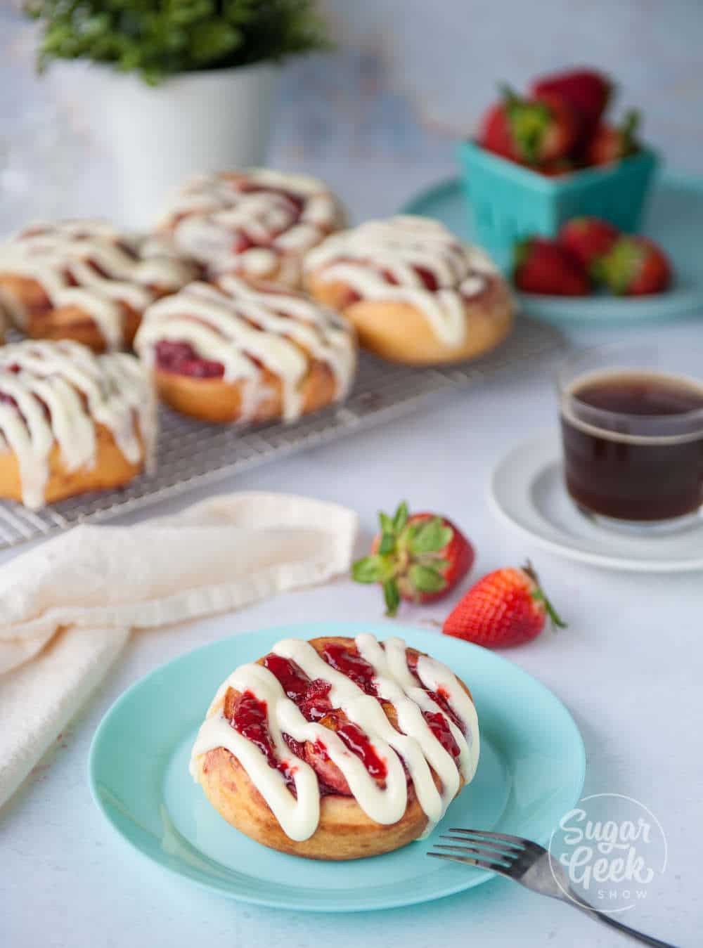 strawberry cinnamon roll on a blue plate with strawberry cinnamon rolls in the background