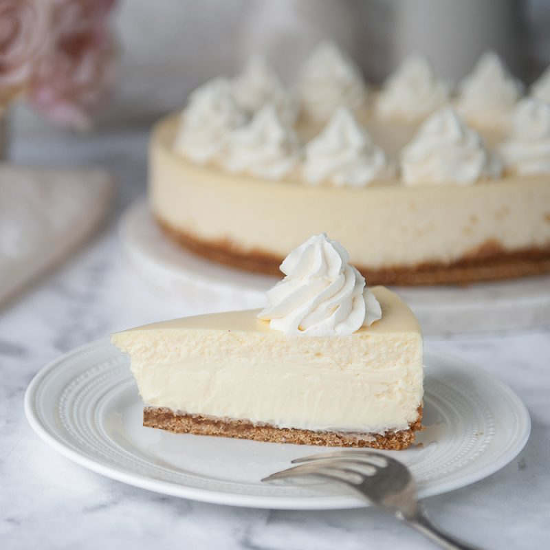 slice of cheesecake on a white plate with whole cheesecake in the background