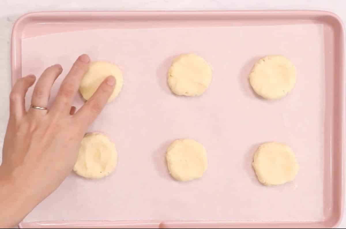 Lofthouse cookie dough rolled into balls and flattened onto a pink cookie sheet.