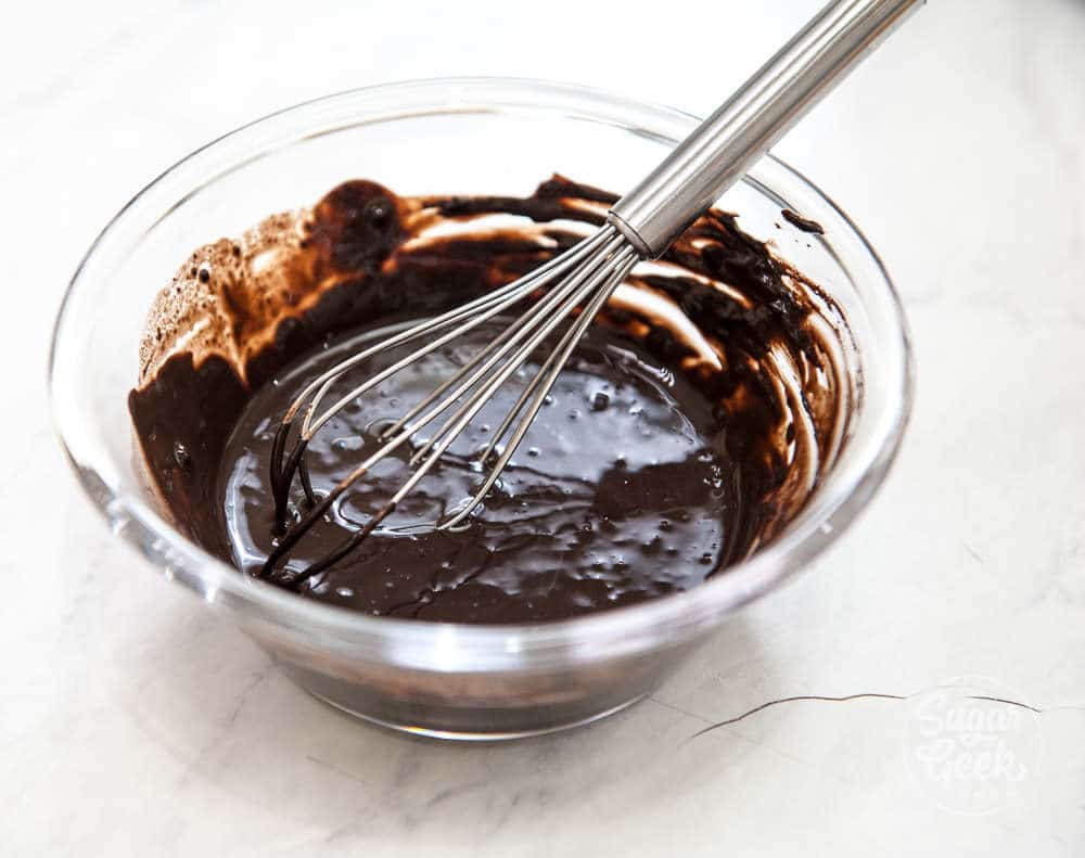 blooming cocoa powder with hot water in a clear bowl and metal whisk