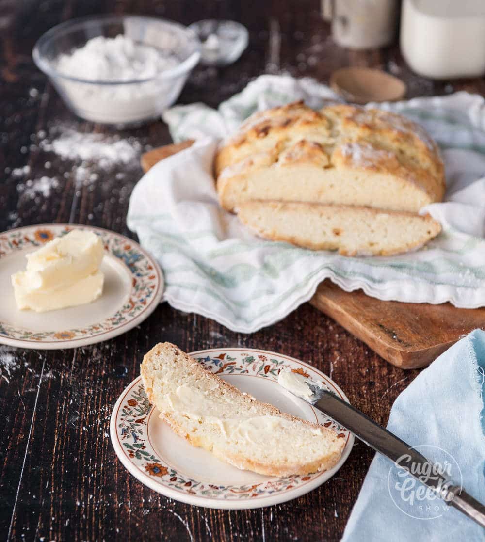 Traditional Irish Soda bread sliced on a plate with butter spread on. Loaf in background