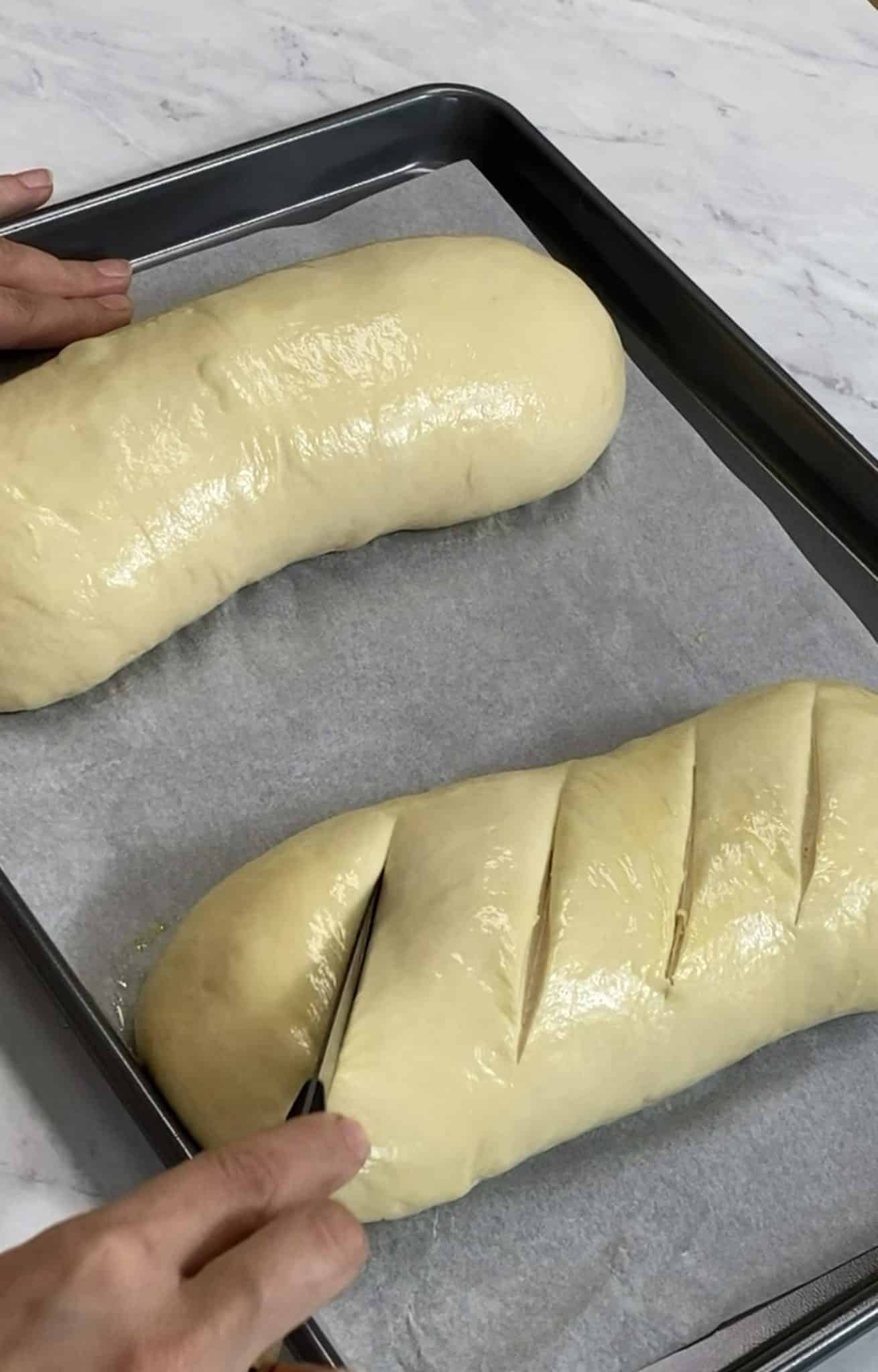 Scoring risen bread dough loaves with a knife.