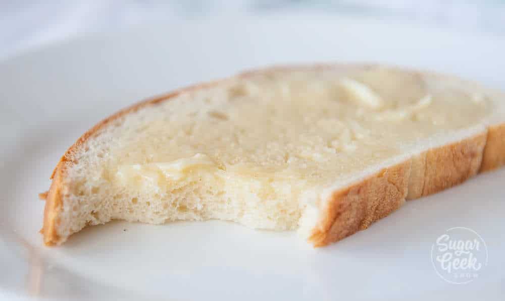 slice of warm homemade bread with butter on top an bite taken out of the bread