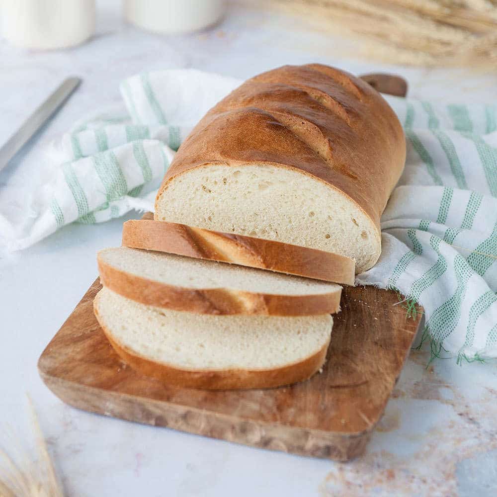 homemade loaf of bread on wooden cutting board with white towel and white background