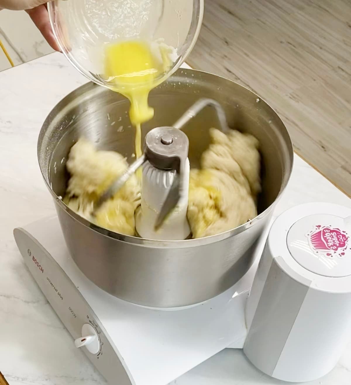 Butter being poured into mixing stand mixer with bread dough.