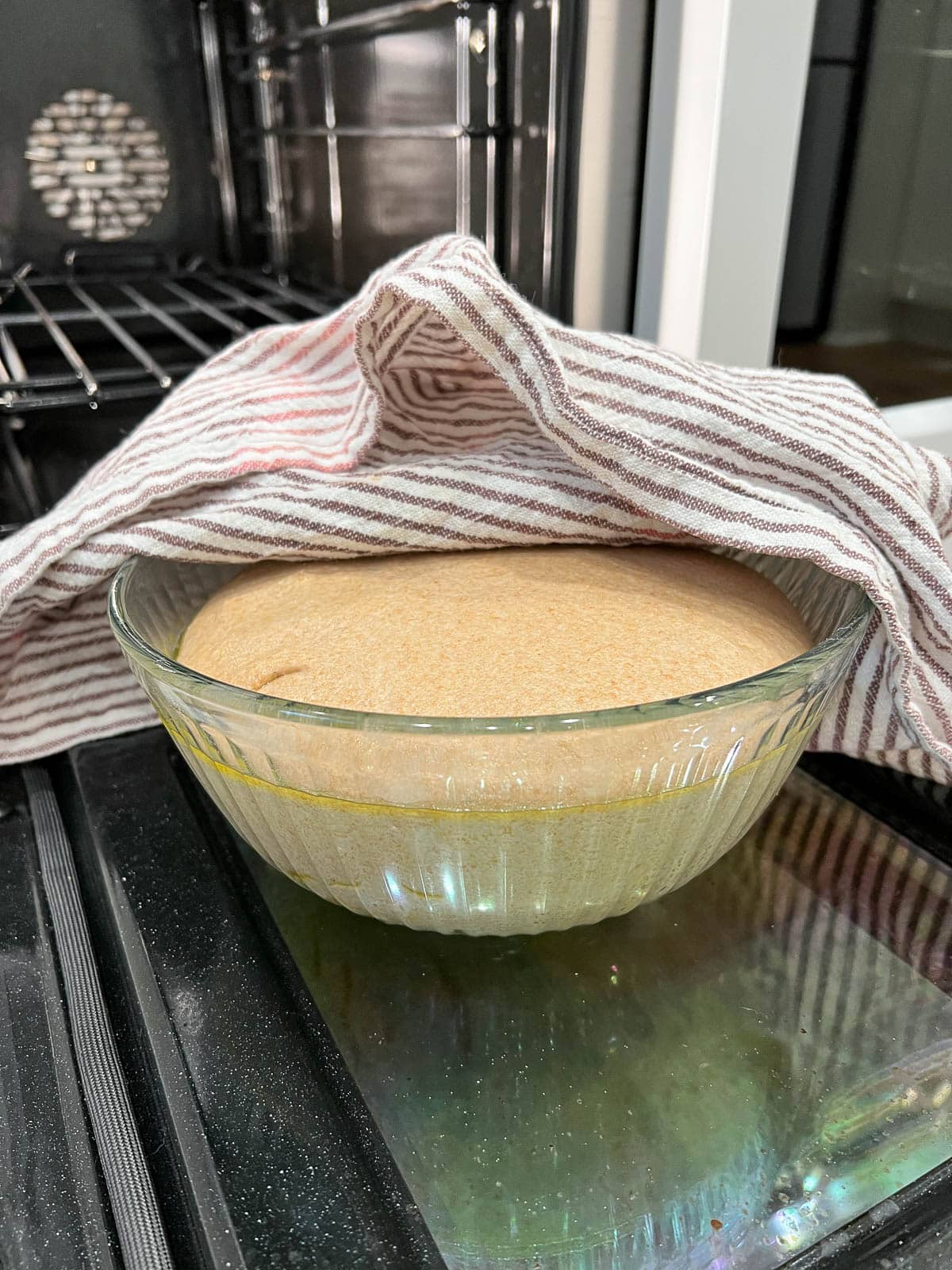 close up of bread dough in a glass bowl in front of an oven