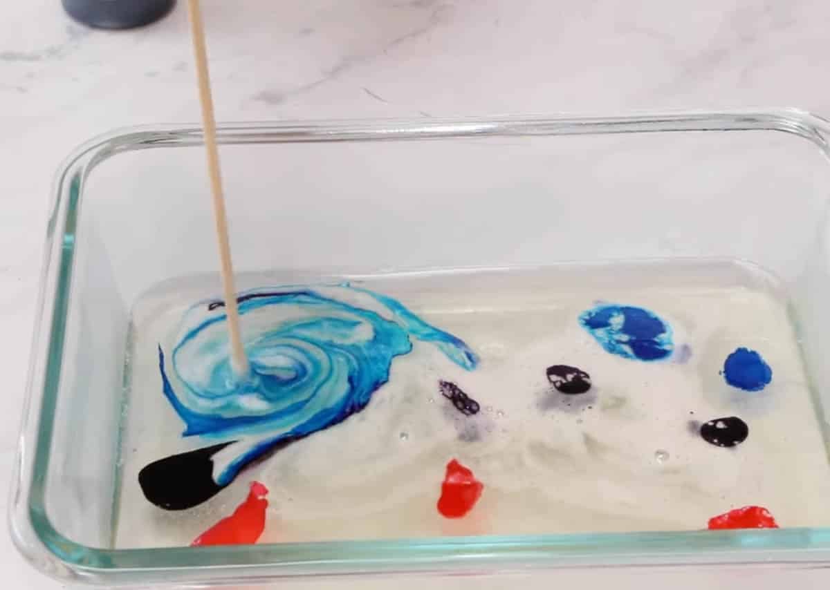 Wooden skewer swirling drops of food coloring into kohakutou mixture.