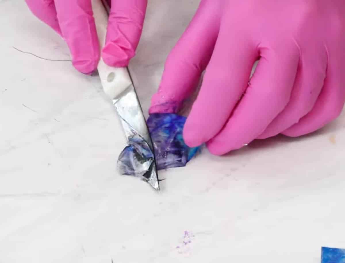 Pink gloved hands cutting kohakutou crystals into gem shapes with a small knife.