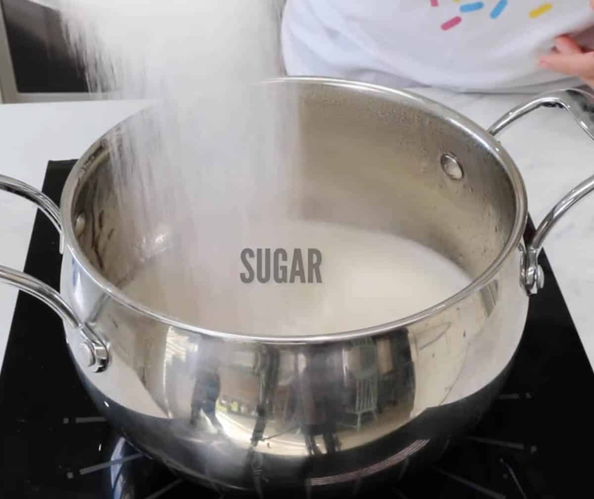 Pouring sugar in agar agar mixture in a metal saucepan.
