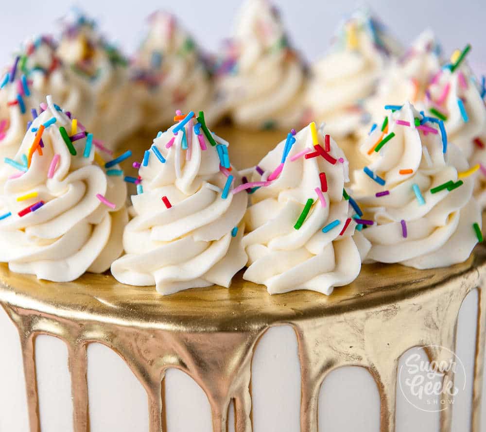 closeup of buttercream frosting on gold drip cake with rainbow sprinkles