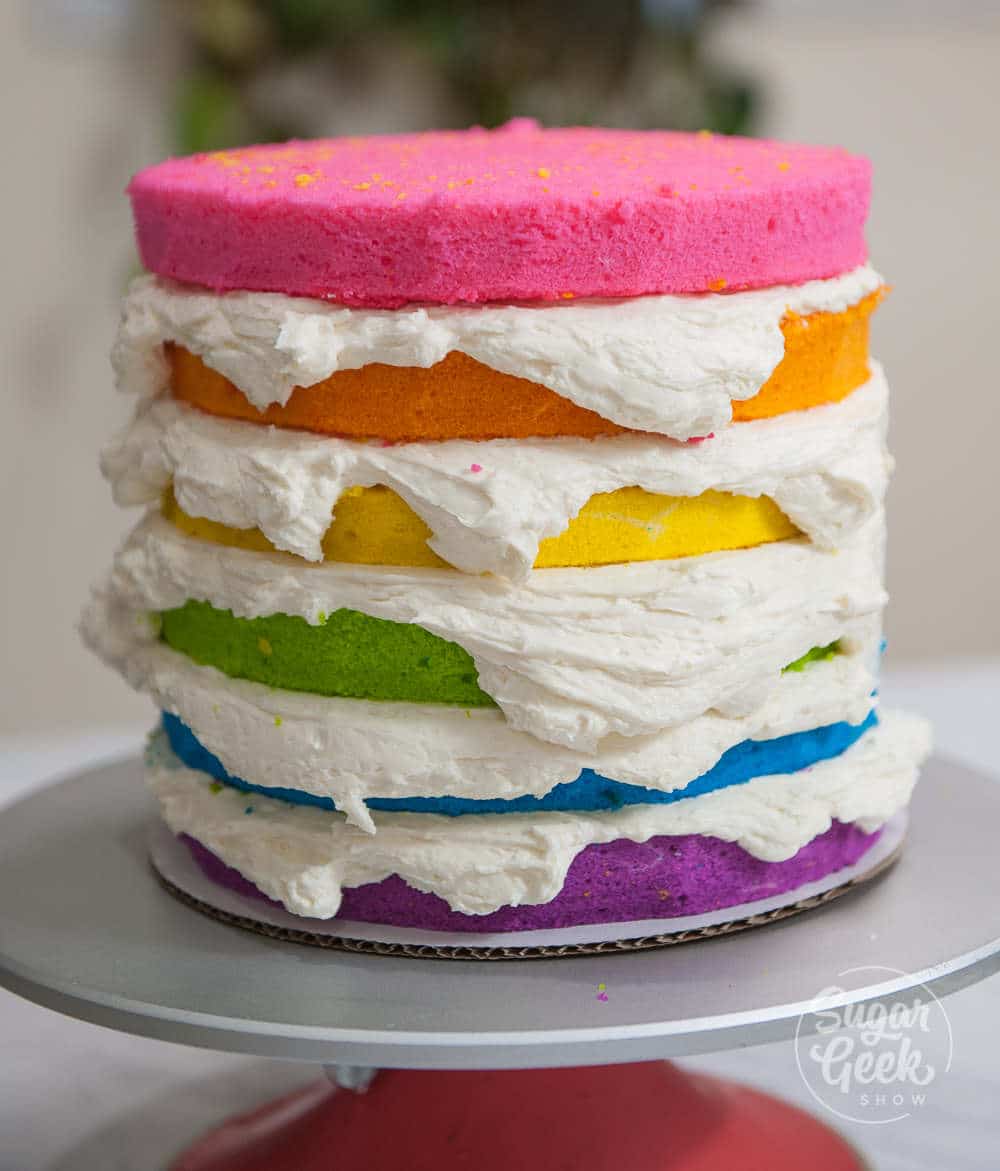 layers of rainbow cake with buttercream frosting in between