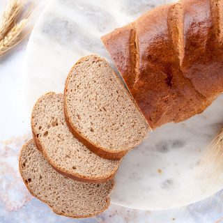 loaf of honey whole wheat bread shot from above with three slices in front on a white background