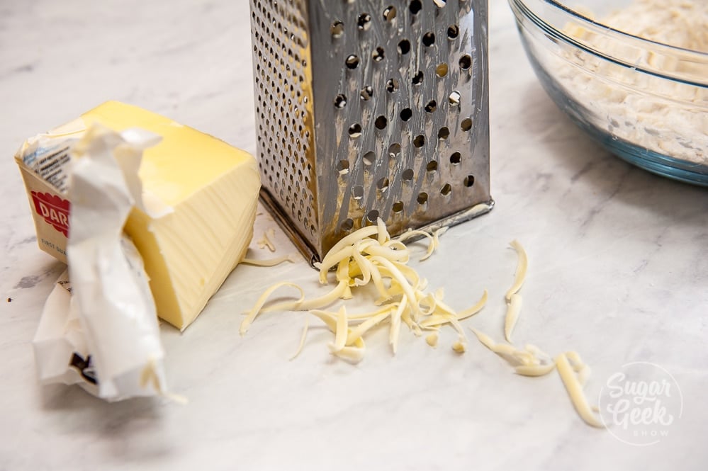 cold grated butter in front of a metal grater on white countertop