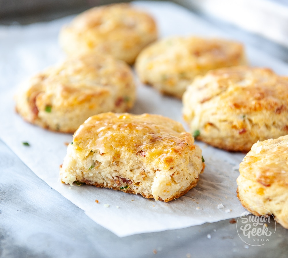 bacon cheddar chive biscuits on white parchment paper on metal baking sheet with a bit taken out of one