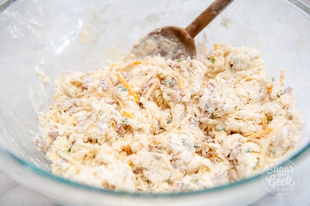 cheddar bacon biscuit ingredients in a clear bowl with wooden spoon