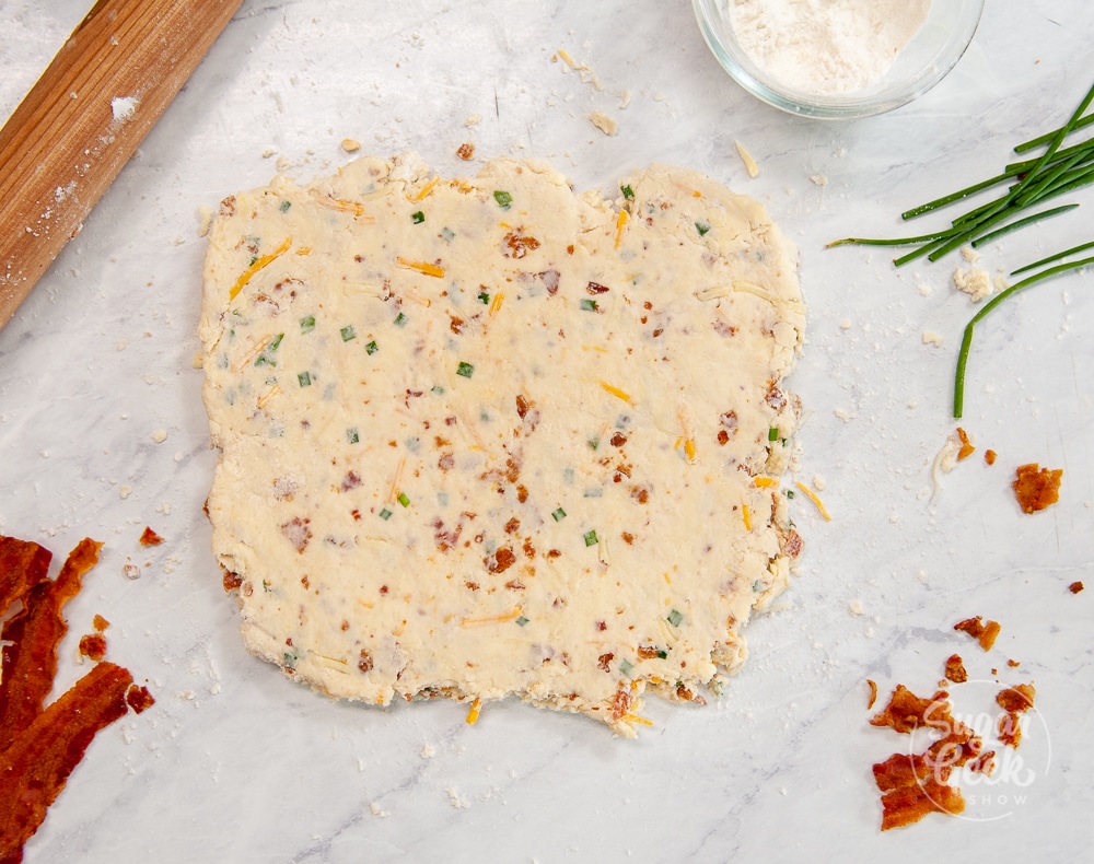 bacon cheddar chive biscuit dough rolled out on. a white background with ingredients surrounding 