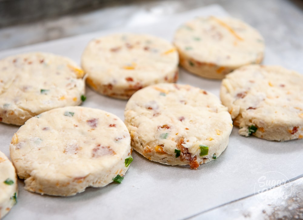 bacon cheddar chive biscuits on parchment paper on a metal baking sheet