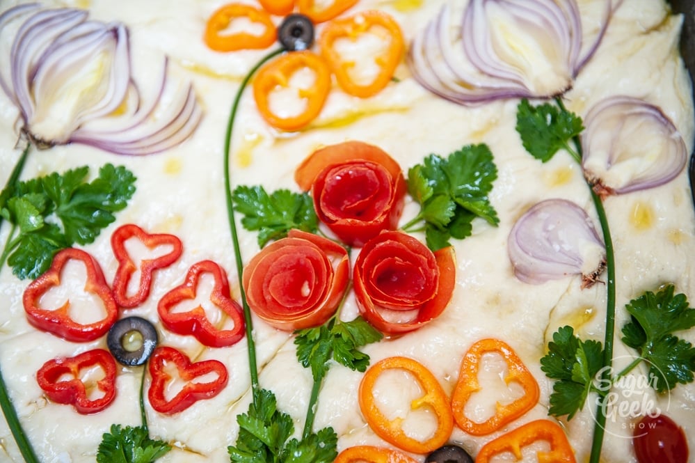 bell peppers, tomato roses, red onions and parsley on raw focaccia dough in the design of flowers