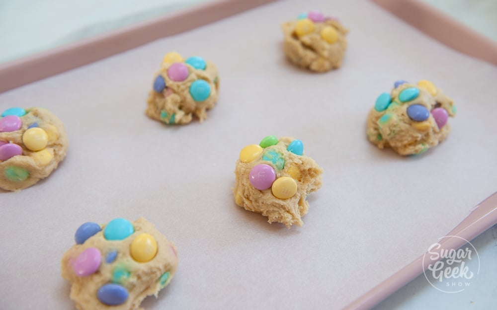 M&M cookie dough balls on a parchment covered cookie sheet