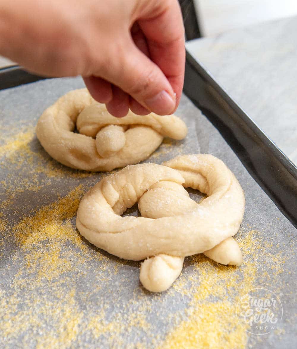 sprinkling salt onto freshly boiled pretzels on parchment paper with cornflour