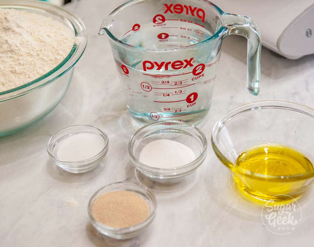 flour, water, sugar, salt, melted butter, yeast in clear bowls on white countertop