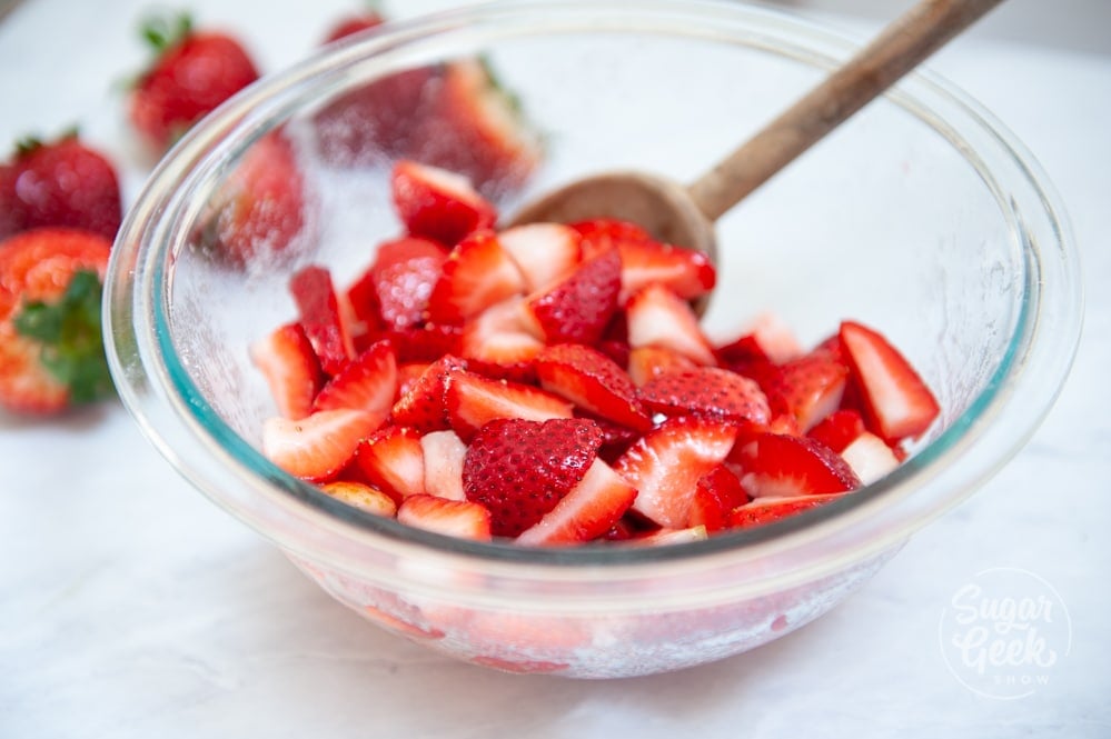 sliced strawberries and sugar in clear bowl with wooden spoon