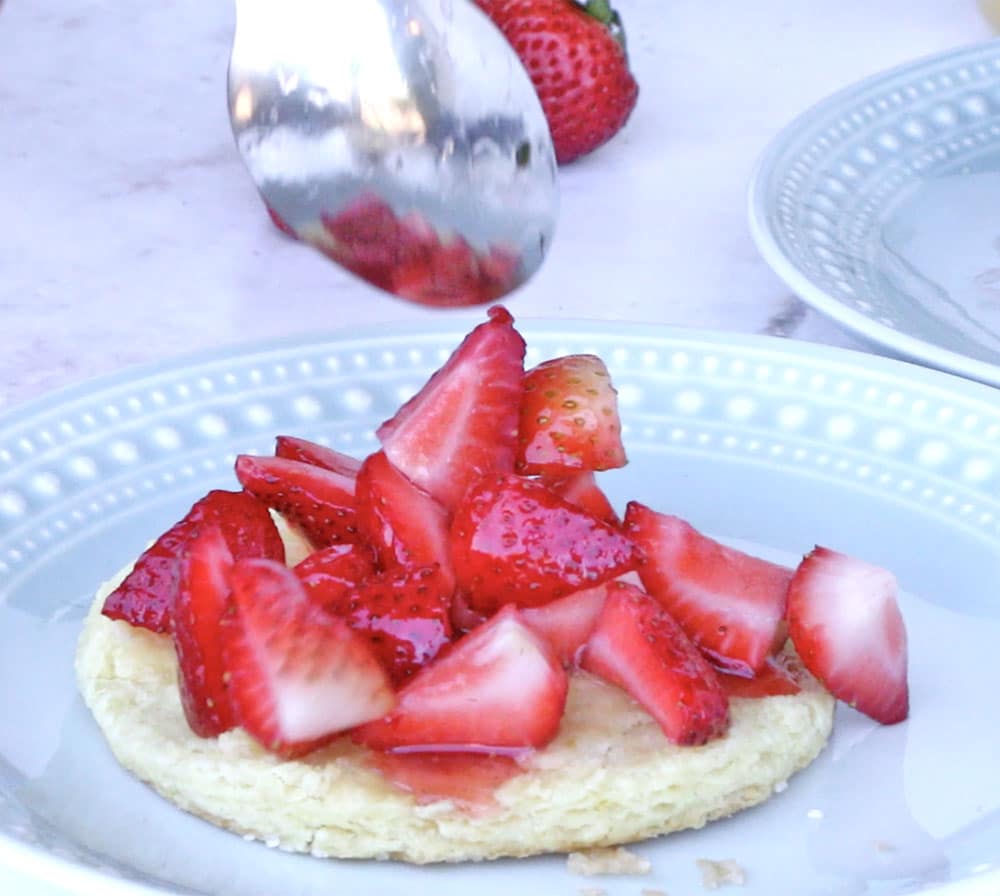 strawberries being spooned onto half of a biscuit