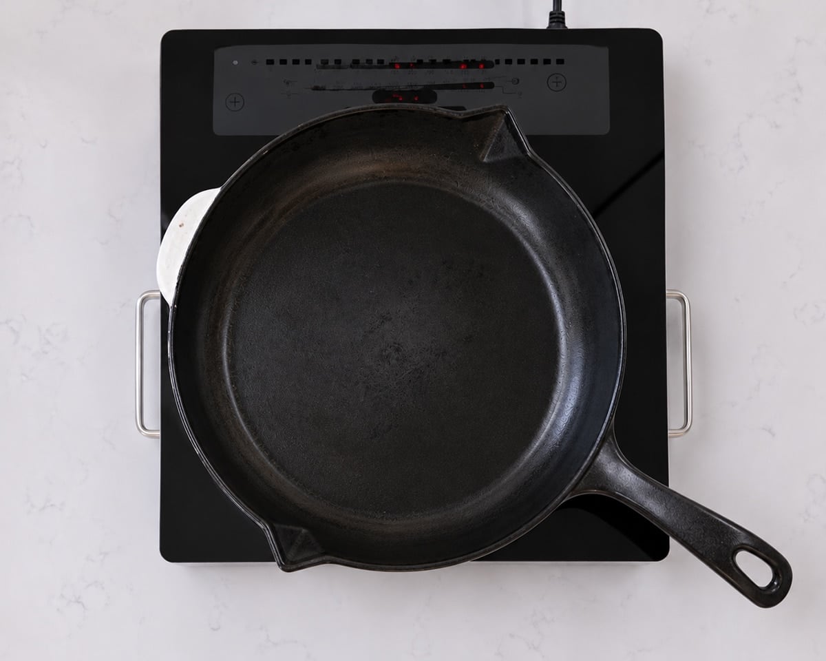 Cast iron skillet heating on a portable electric cooktop.
