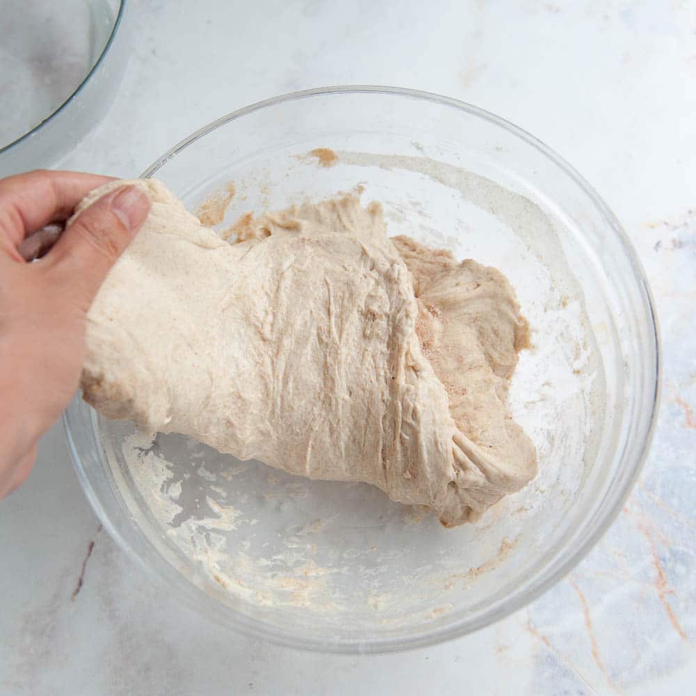 Hand pulling sourdough dough out of a clear glass bowl.