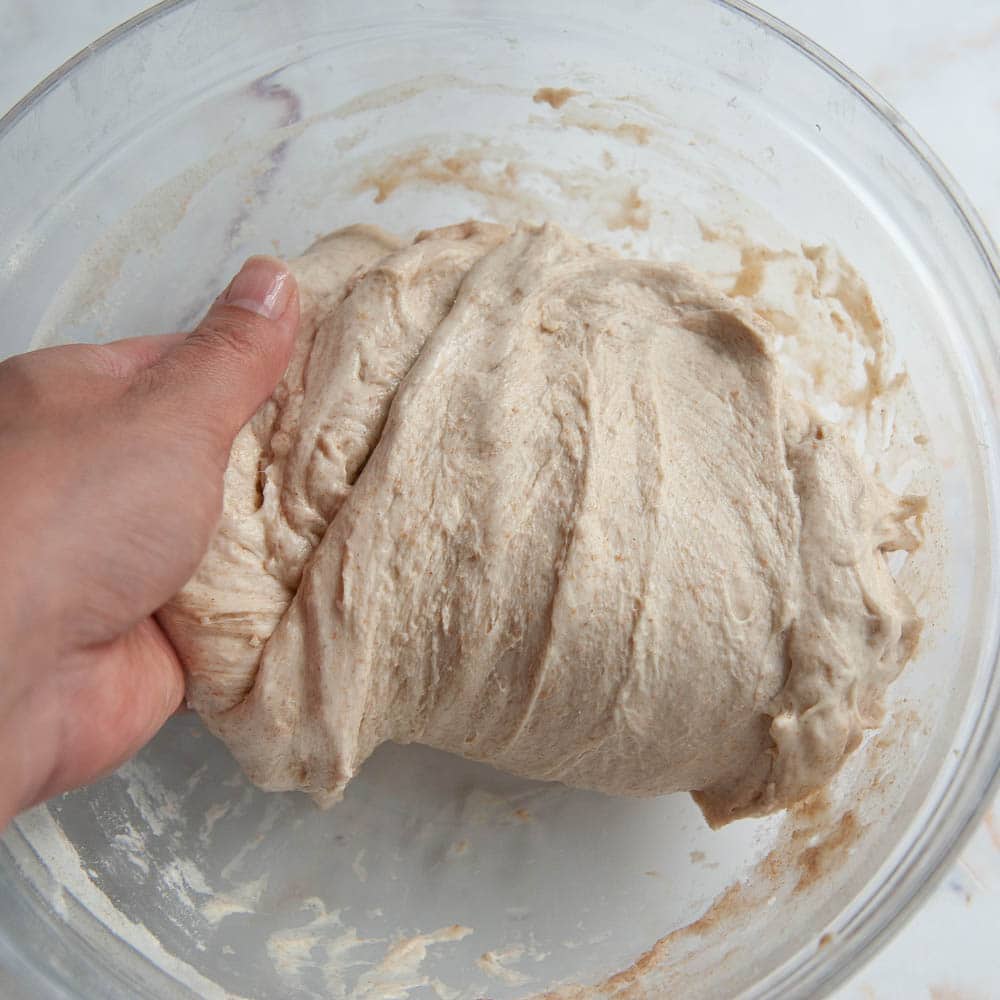 unbaked dough in a clear bowl with hand