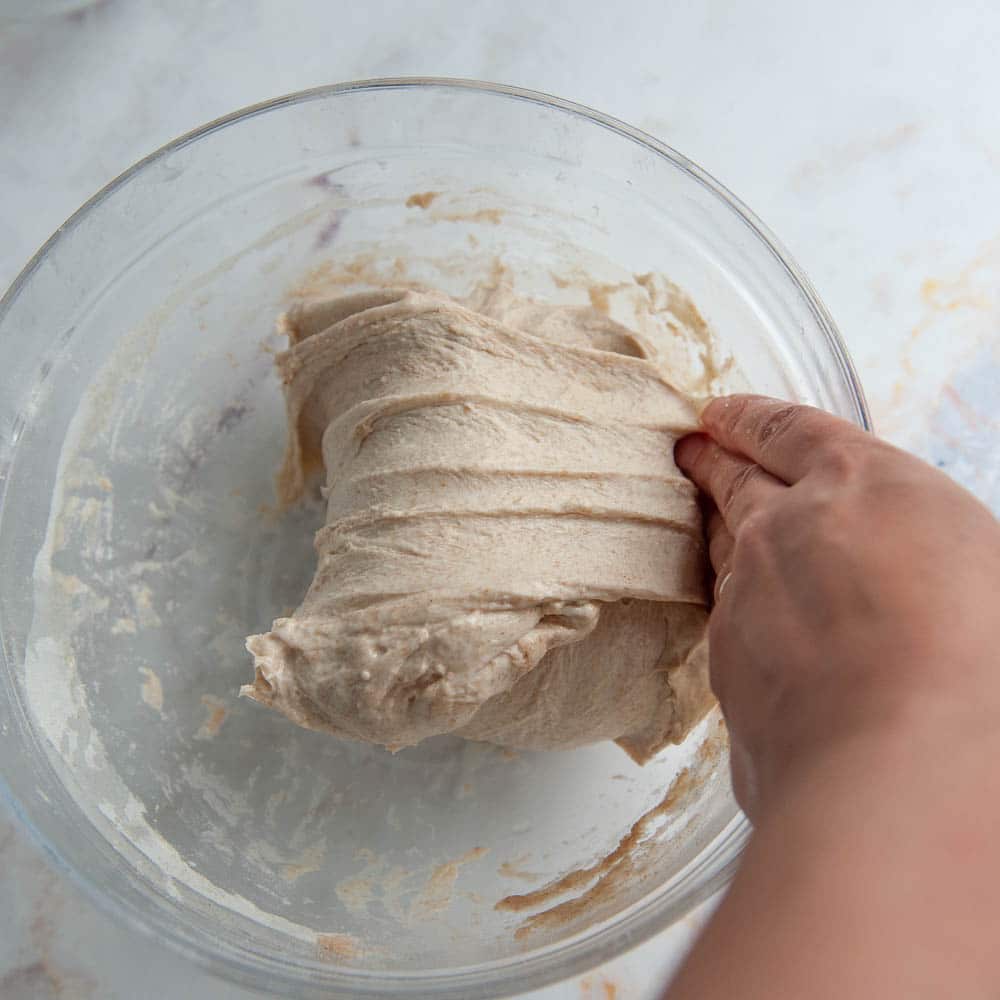 hand folding wet dough over in a clear bowl