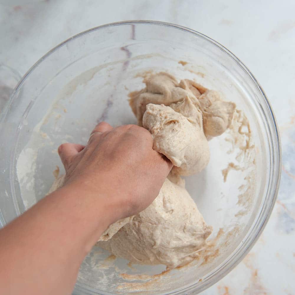 mixing sourdough with hands in a clear bowl