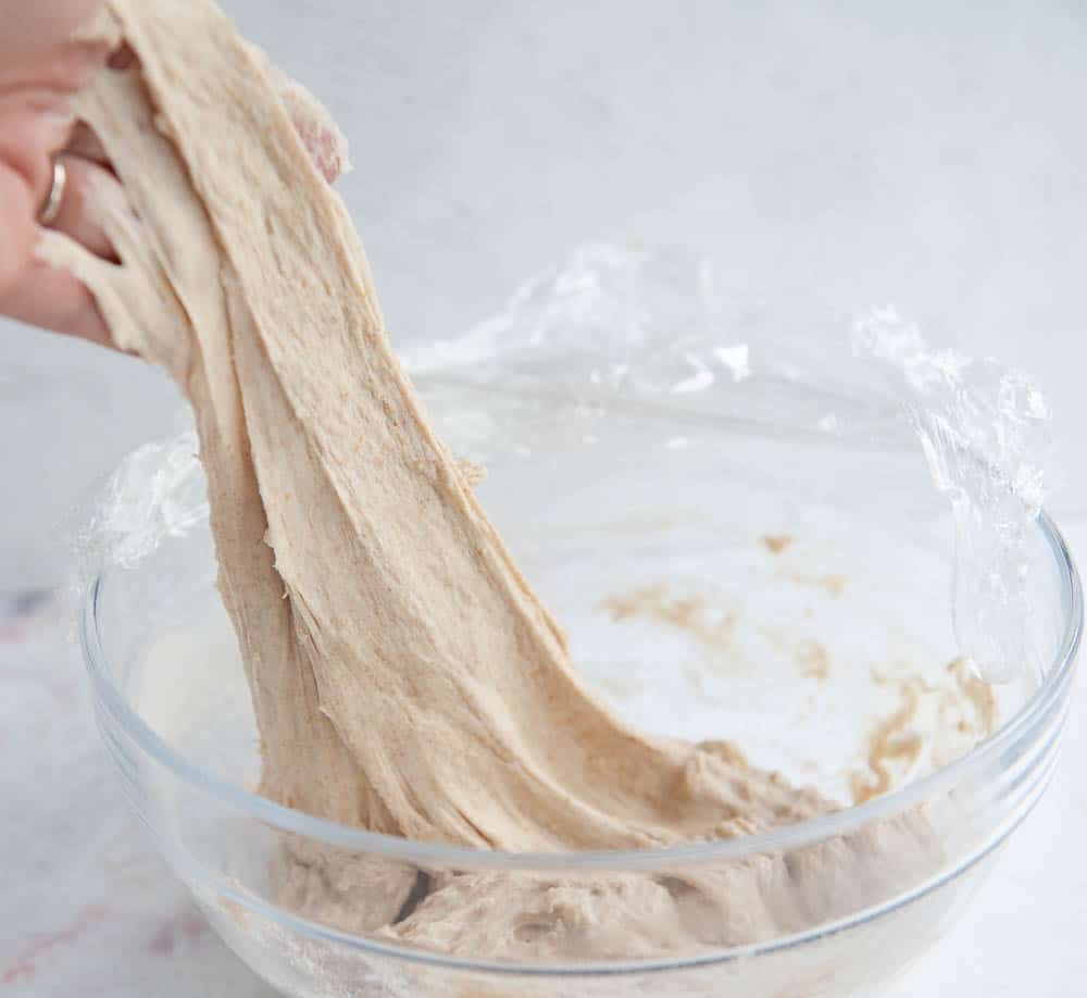 hand reaching into a clear glass bowl of sourdough and pulling it up.