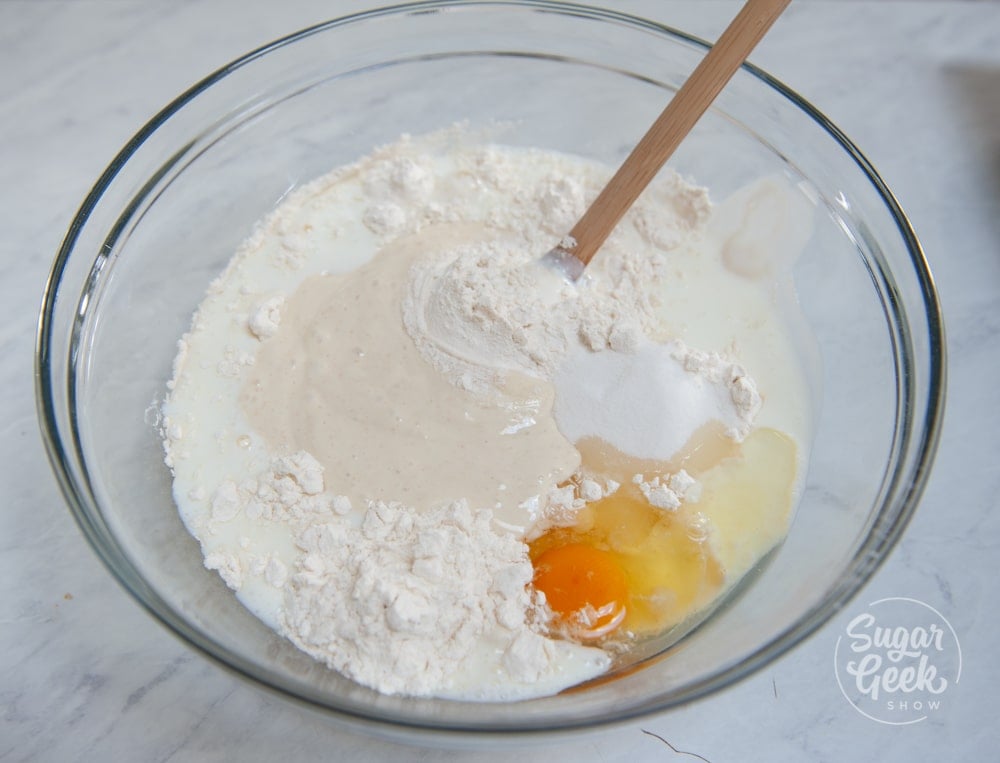 sourdough pancake ingredients in a clear bowl with a wooden spoon