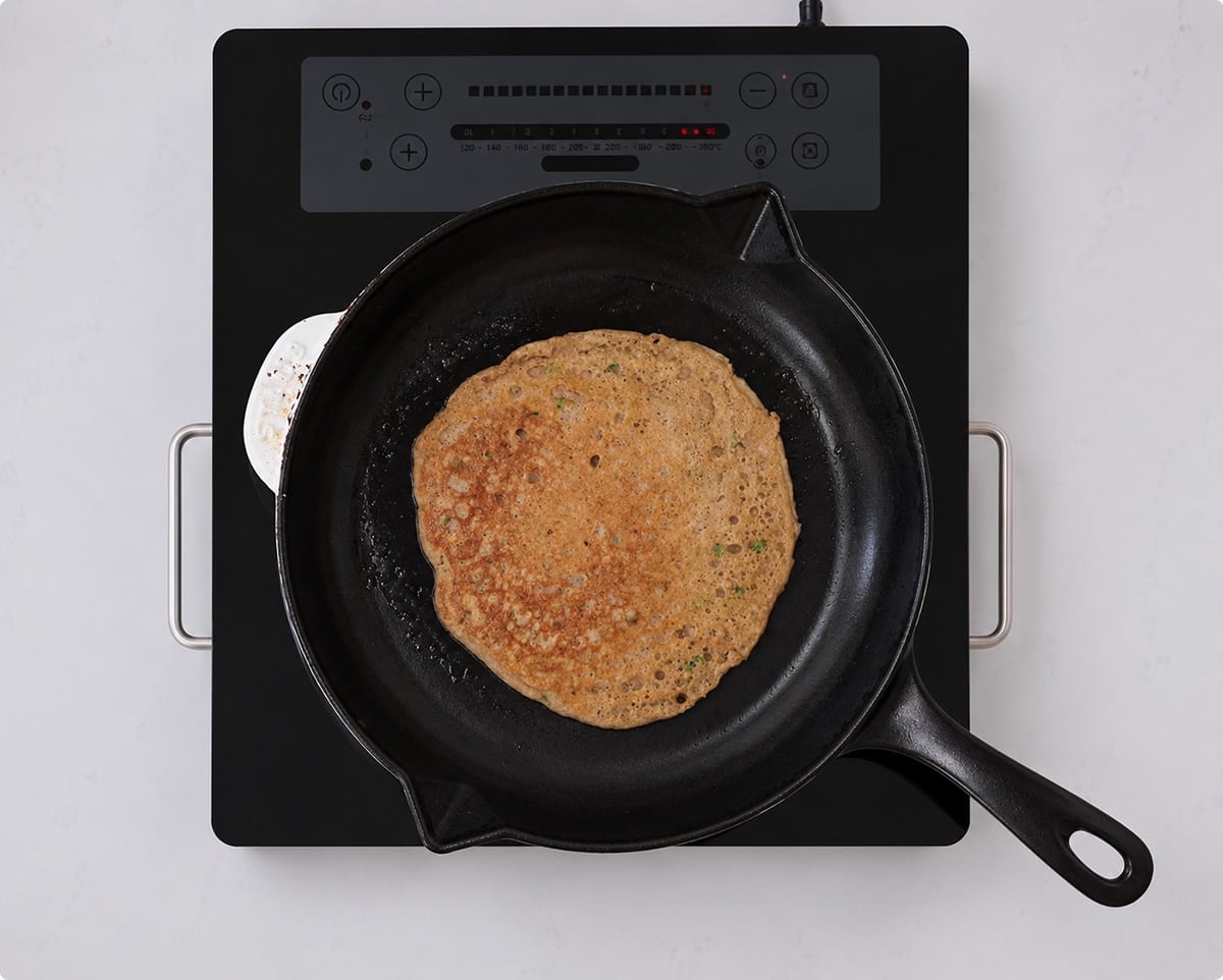 Sourdough pikelet cooking in a hot cast iron pan.