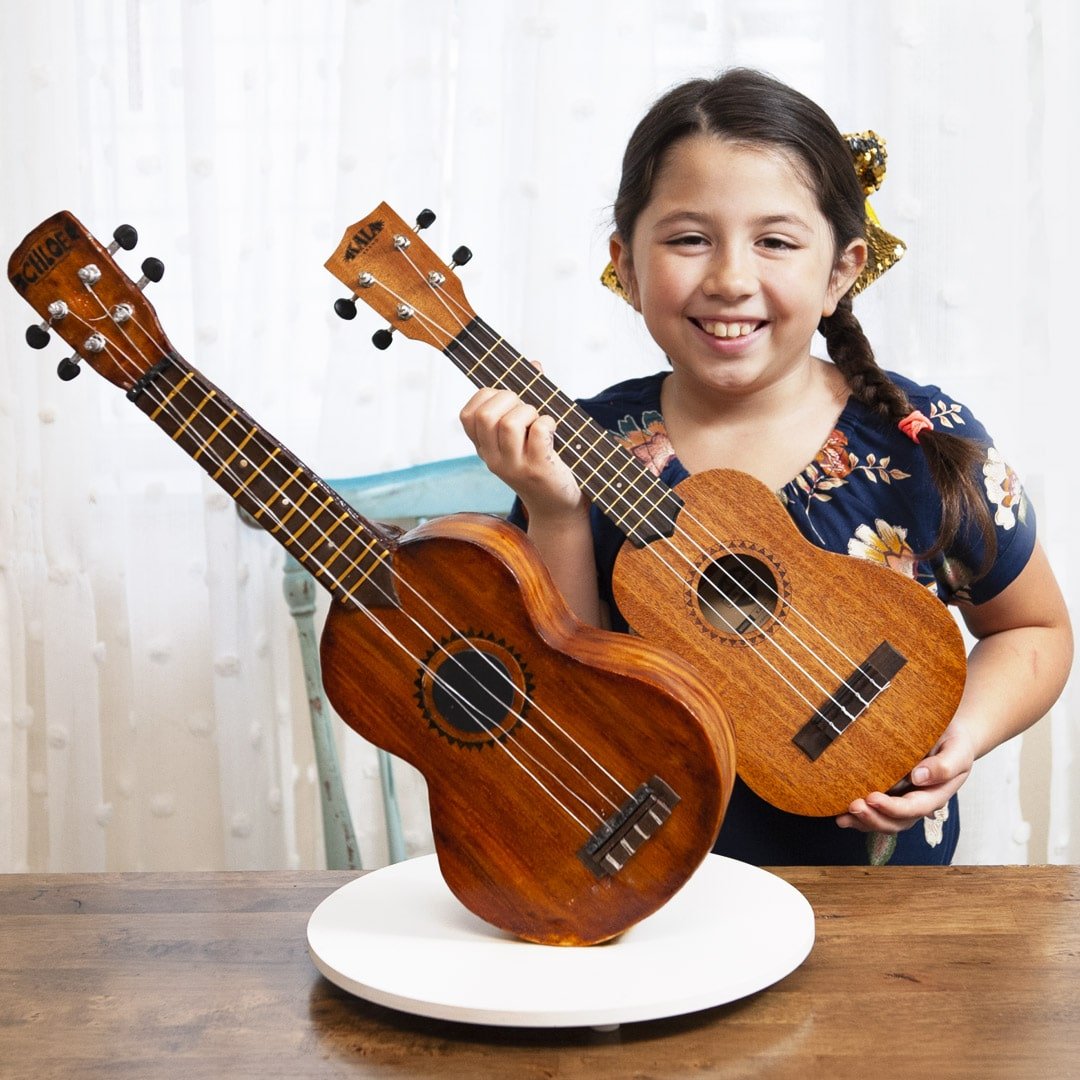 Ukulele Cake standing upright with girl holding ukulele behind to show how similar they are