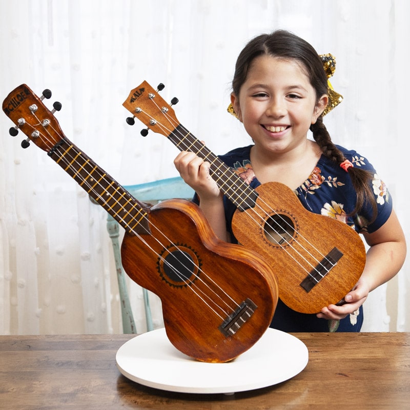 Ukulele Cake standing upright with girl holding ukulele behind to show how similar they are