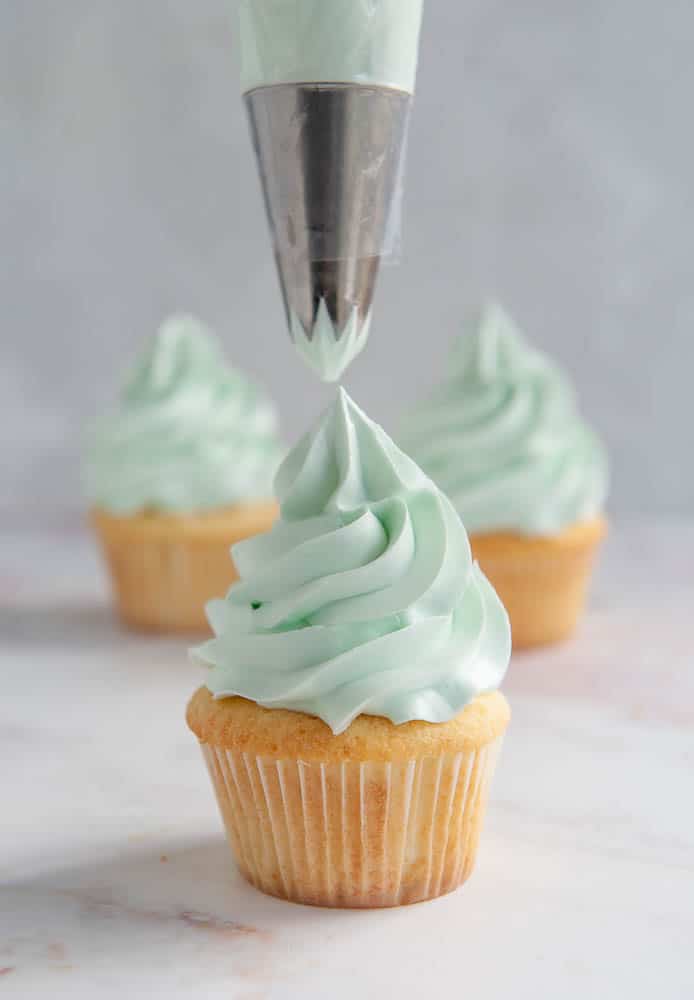 piping frosting onto vanilla cupcake