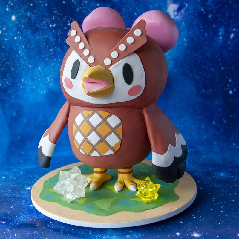 Cake sculpted into the shape of Animal Crossing character Celeste standing on a green grass cake board with isomalt star shapes