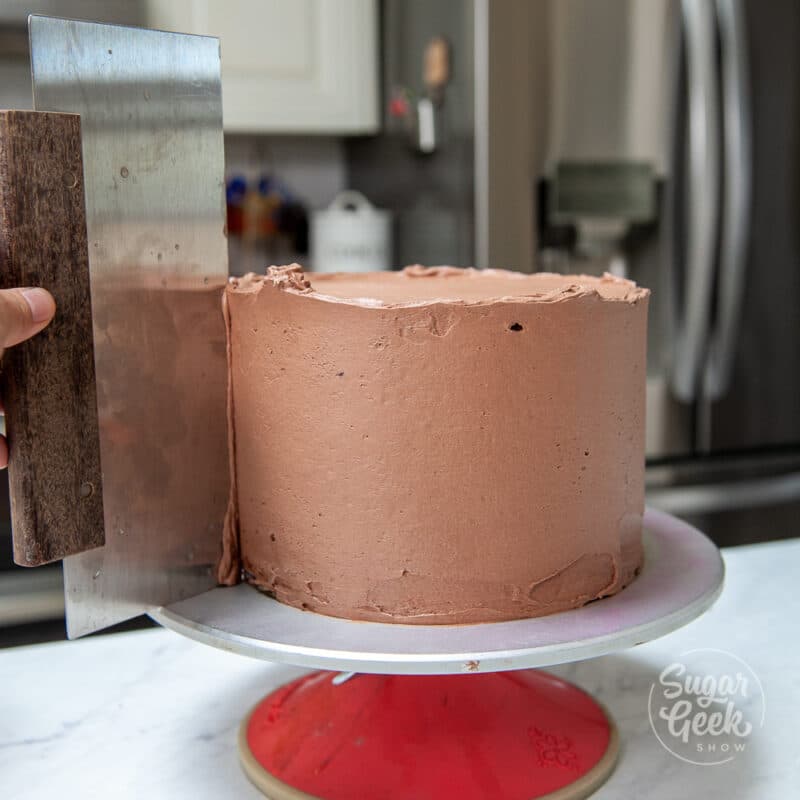 bench scraper smoothing the side of the chocolate cake