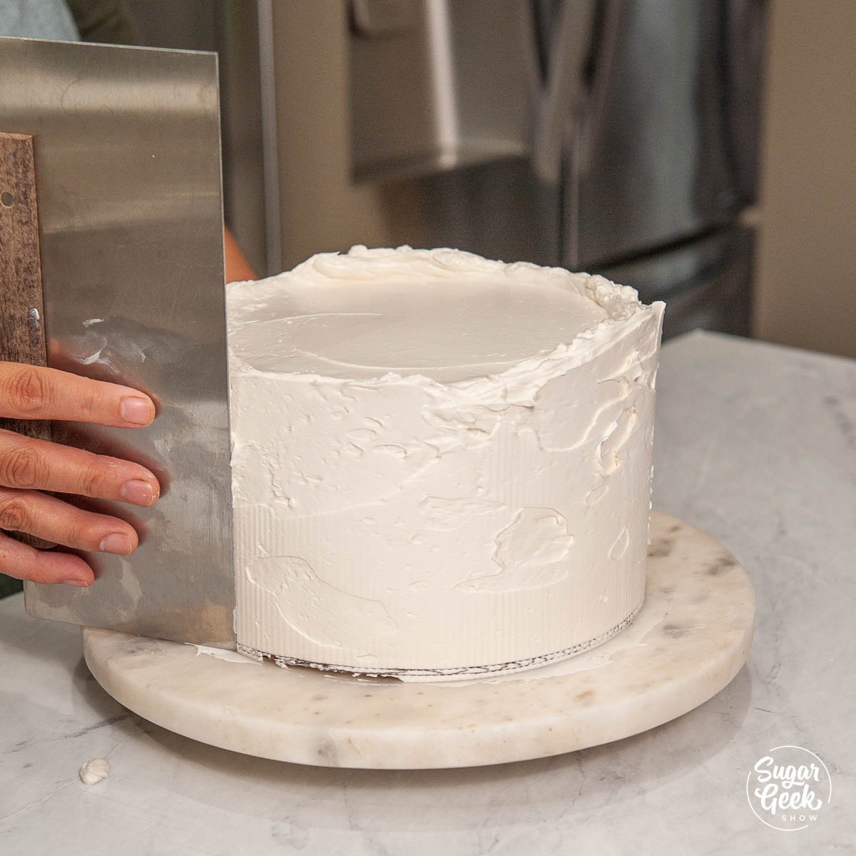 smoothing the final layer of buttercream with a bench scraper