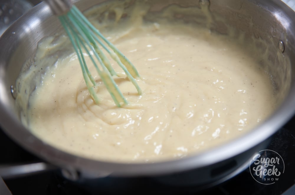 closeup of thickened pastry cream in metal pot with blue whisk