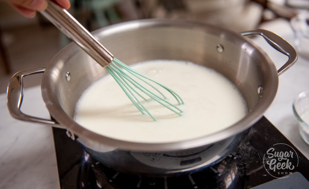whisking pastry cream ingredients in stainless steel pot with blue whisk
