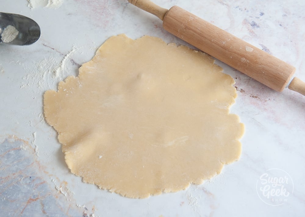 tart dough rolled out on a white background with wooden rolling pin