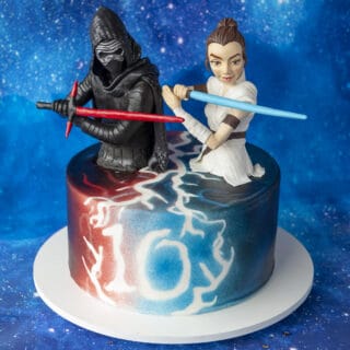 Birthday cake colored with red and blue edible airbrush color with sculpted Rey and Kylo Ren cake toppers holding lightsabers